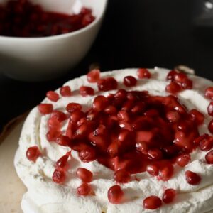 Pavlova topped with whipped cream and pomegranate