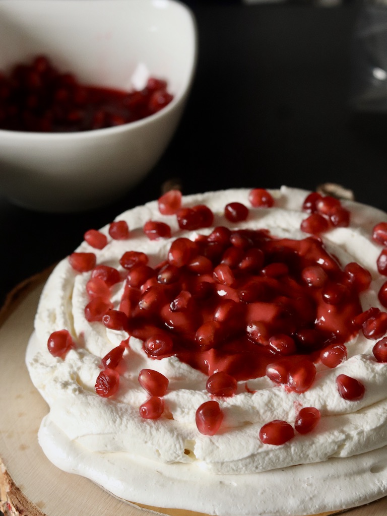 Pavlova topped with whipped cream and pomegranate