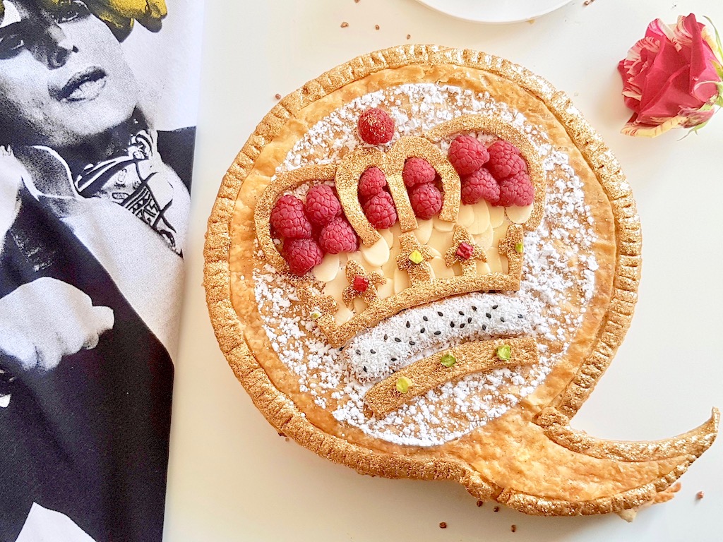 Galette des rois topped with puff pastry crown design almonds and raspberries next to Freddie Mercury Tshirt