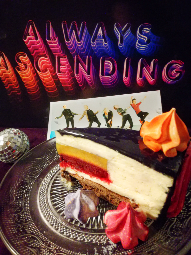 Slice of mirror glaze cake with mango and raspberry insert next to Franz Ferdinand Always Ascending vinyl record