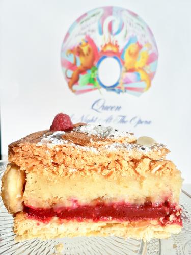 Galette des rois slice puff pastry generous frangipane cream and raspberry cream next to Queen A Night At The Opera vinyl record
