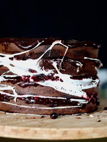 Chocolate layer cake filled with red berries wrapped in marshmallow web